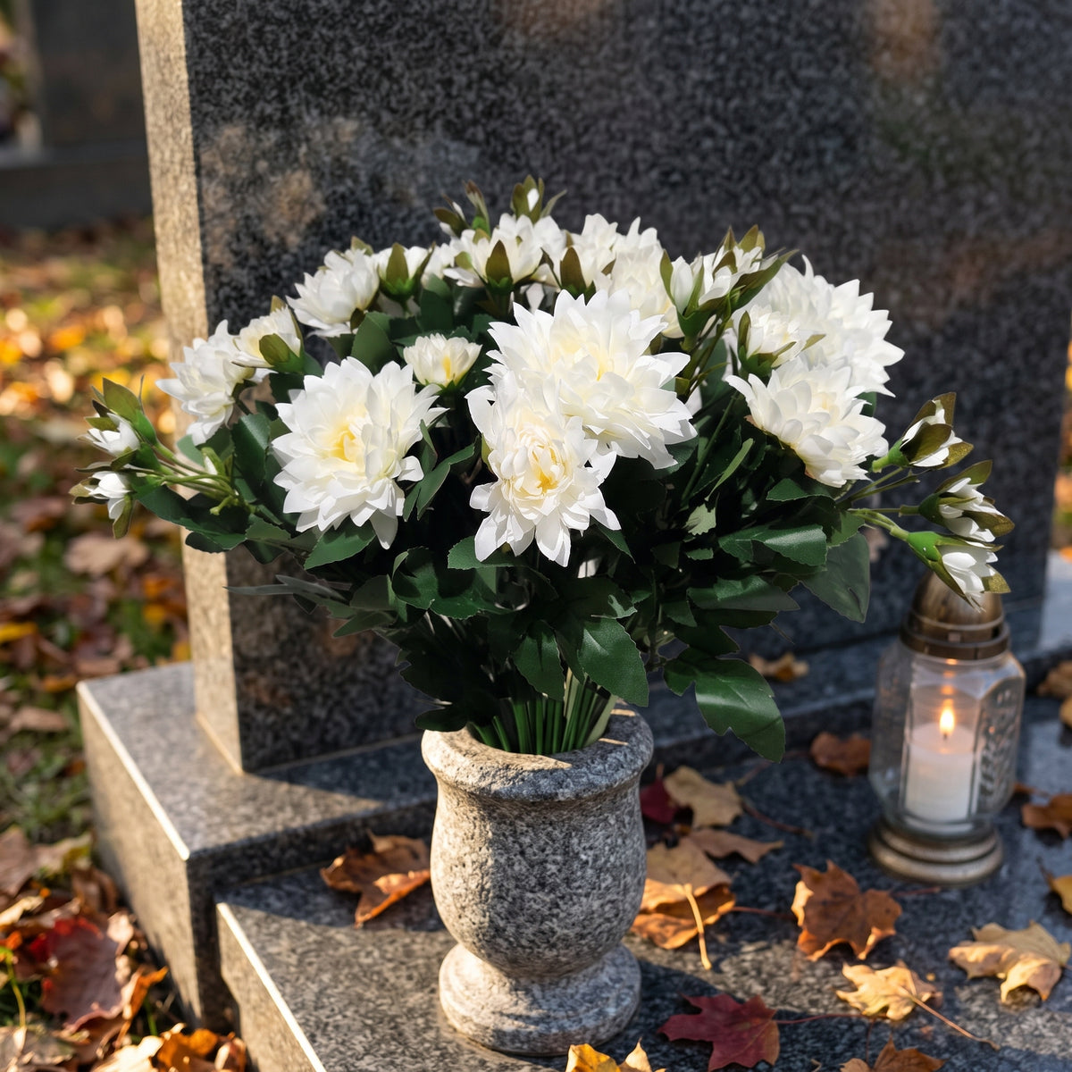 Bukiet białych chryzantem przy nagrobku ze zniczem, jesienne liście